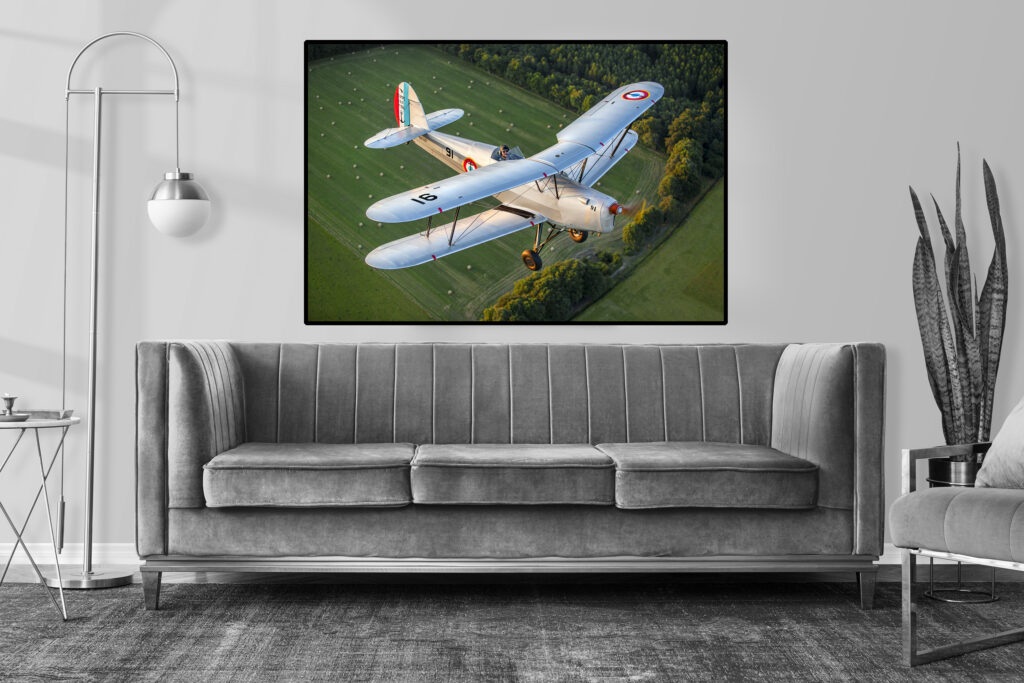 Photographie d'un avion biplan Stampe SV4 en vol au dessus de la campagne - Photo de Pascal Picard. Photo de Pascal Picard. Mise en situation dans un salon.